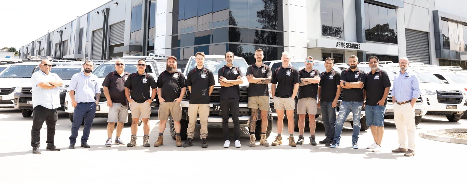 The APMG Services crew standing in a line in front of the company's vans and utes